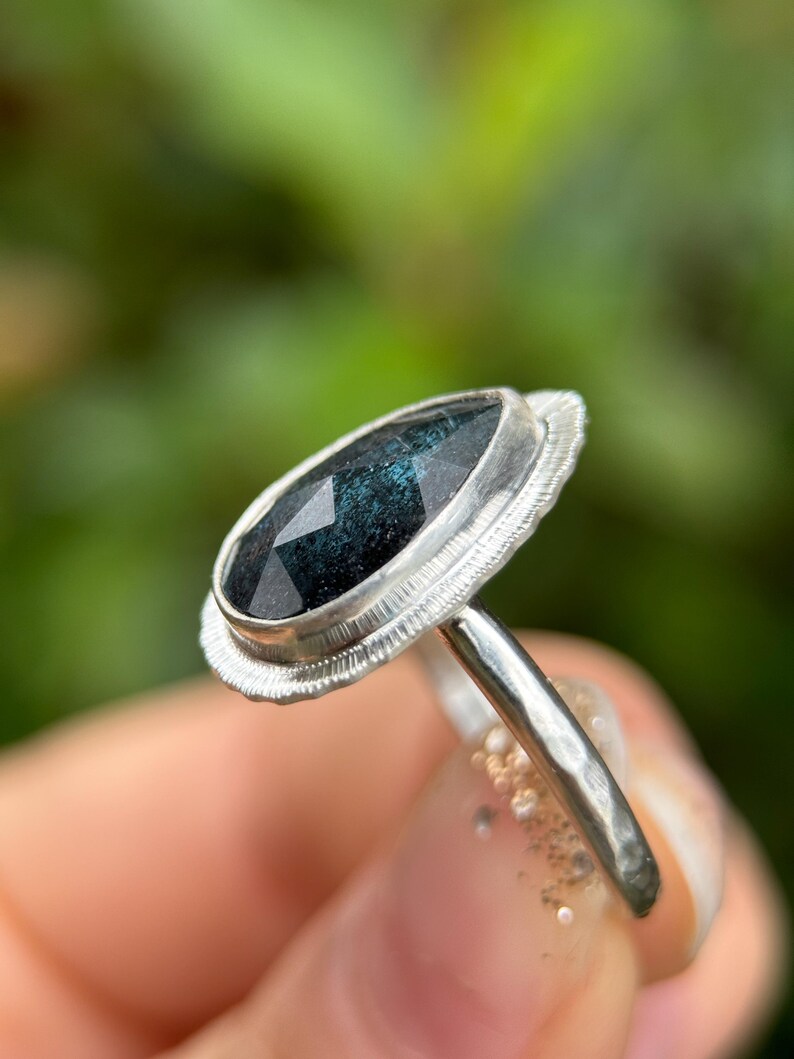 May include: A silver ring featuring a pear-shaped dark green gemstone set in a bezel setting. The ring has a textured band.
