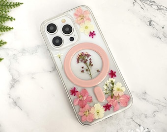 May include: A clear phone case with a pink ring holder and pressed flowers. The flowers are pink, white, and yellow.