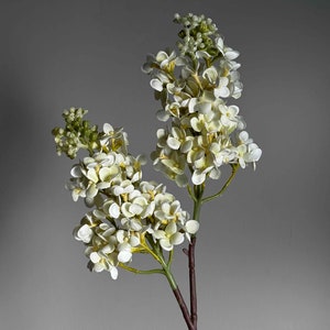 May include: A bouquet of white artificial flowers with green stems and leaves. The flowers are clustered together in a bunch, creating a full and lush look.
