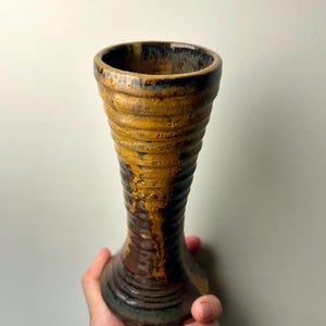 May include: A brown and yellow ceramic vase with a textured, ribbed design. The vase has a narrow neck and a wide base.