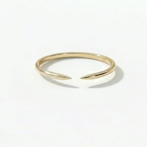 May include: A gold ring with an open design. The ring is made of polished gold and features two pointed ends that do not meet, creating an open space. The ring is set against a white background.