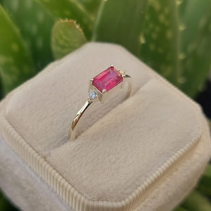 May include: A silver ring with a pink emerald-cut gemstone and two smaller clear gemstones.