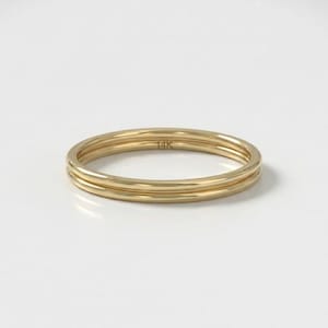 Op de afbeelding: Een gouden ring met een drievoudig bandontwerp. De ring is gemaakt van gepolijst goud en heeft de markering "14K". De ring staat tegen een witte achtergrond.