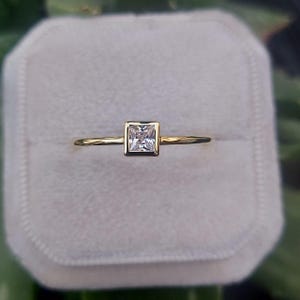 Peut inclure: Une bague simple en or avec une pierre précieuse transparente de forme carrée sertie dans une bélière en or.