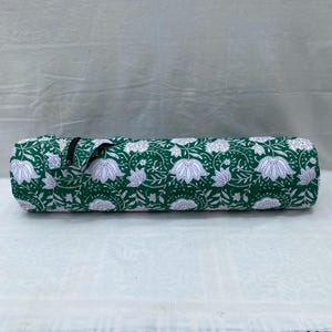 K&ouml;nnte beinhalten: Eine zylindrische Yogamatten-Tasche. Die Tasche hat einen gr&uuml;nen Hintergrund mit einem wei&szlig;en Blumenmuster. Sie hat einen schwarzen Rei&szlig;verschluss und einen Griff. Die Tasche ist f&uuml;r den Transport einer Yogamatte und anderem Zubeh&ouml;r konzipiert.