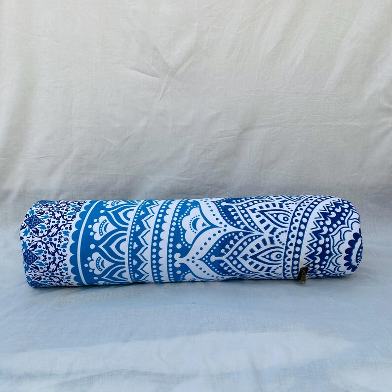 May include: A cylindrical bolster pillow with a blue and white mandala pattern. The pillow has a zipper closure and is made of fabric. The design features intricate floral and geometric elements, creating a decorative and functional item.