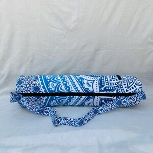 May include: A blue and white yoga mat bag with a decorative mandala pattern. The bag has a black zipper and a matching shoulder strap. The bag is designed to carry a rolled-up yoga mat.