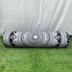 May include: A cylindrical bolster pillow with a black and white mandala design. The pillow is long and features intricate geometric patterns. The pillow is resting on green grass.