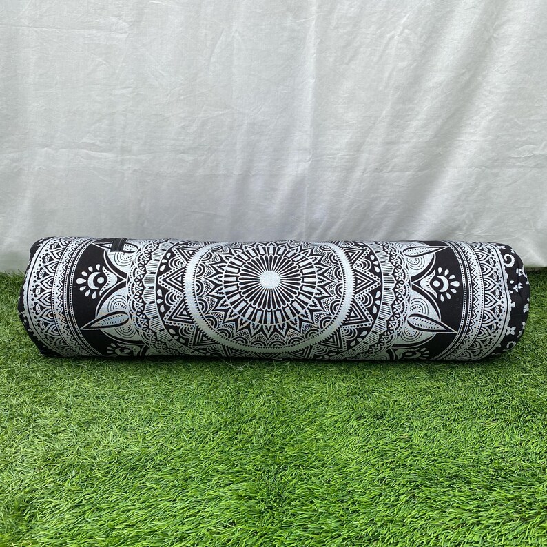 May include: A cylindrical bolster pillow with a black and white mandala design. The pillow is long and features intricate geometric patterns. The pillow is resting on green grass.
