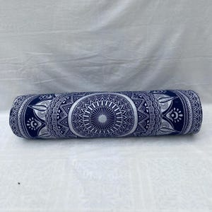 May include: A rolled yoga bolster with a navy blue background and a white mandala pattern. The bolster is cylindrical and features an intricate, symmetrical design. The ends of the bolster have an eye-like design.