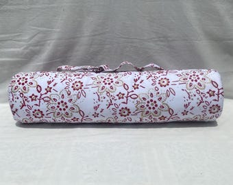 May include: A cylindrical yoga bolster with a white background and a repeating floral pattern in burgundy and gold. The bolster has a matching handle for easy carrying. The design is a mix of floral and leaf shapes.