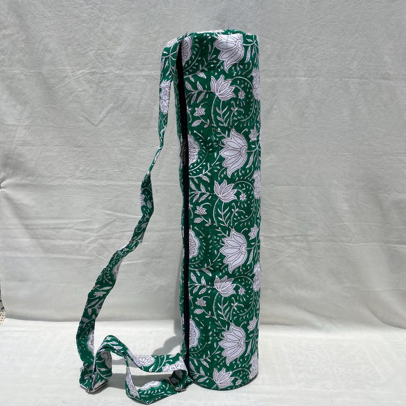 K&ouml;nnte beinhalten: Gr&uuml;ne Yogamatten-Tasche mit wei&szlig;em Blumenmuster. Die Tasche hat einen langen Trageriemen und einen schwarzen Rei&szlig;verschluss. Das florale Design umfasst Lotusblumen und Bl&auml;tter. Die Tasche ist aus Stoff.