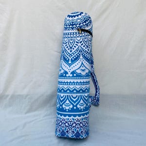 May include: A blue and white yoga mat bag with a decorative mandala pattern. The cylindrical bag has a zipper closure and a shoulder strap. The bag is made of fabric and is designed to carry a yoga mat.