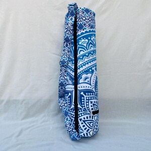May include: A rolled-up yoga mat in a blue and white patterned carrying case. The case features a detailed, symmetrical design with a black zipper and a matching strap. The color scheme is predominantly blue and white.