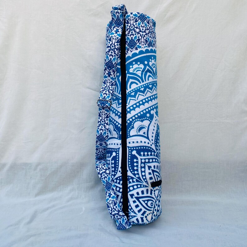 May include: A rolled-up yoga mat in a blue and white patterned carrying case. The case features a detailed, symmetrical design with a black zipper and a matching strap. The color scheme is predominantly blue and white.