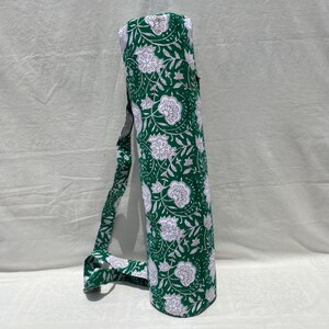 K&ouml;nnte beinhalten: Gr&uuml;ne Yogamatten-Tasche mit wei&szlig;em Blumenmuster und passendem Schultergurt. Die zylindrische Tasche ist f&uuml;r den Transport einer zusammengerollten Yogamatte konzipiert. Der Stoff hat ein sich wiederholendes Muster aus stilisierten Blumen und Bl&auml;ttern.