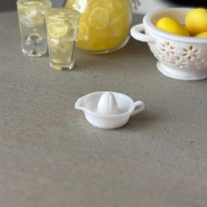 May include: A white plastic citrus juicer with a pointed top and a handle on the side. The juicer is sitting on a gray countertop.