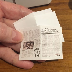 May include: A miniature newspaper called "The Daily News" with the headline "My Mom From Porch" and a picture of a money bag with a dollar sign on it.
