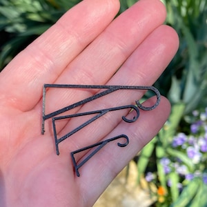 May include: Three black metal hooks of varying sizes. The hooks are all in the shape of a simple triangle with a rounded end.