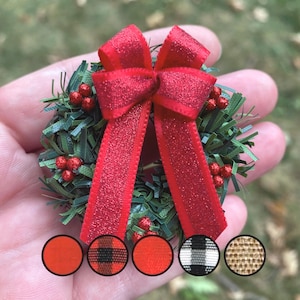 May include: Small Christmas wreath featuring a red glitter bow and red berry decorations. The wreath is green with red berries and a red bow. The image also shows colour swatches of red, plaid, and neutral tones.