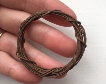May include: A brown, twisted, paper cord, wound into a circle, held in a hand.