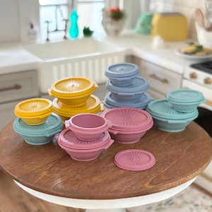 May include: A set of colorful plastic storage containers in yellow, blue, and pink. The containers are stacked and arranged on a wooden table.