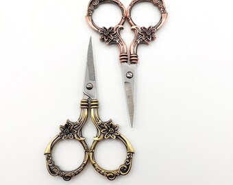 May include: Two pairs of decorative scissors with ornate handles. One pair is gold with a floral design, the other is copper with a floral design.