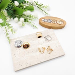 May include: A set of gold and silver earrings and rings with a dotted pattern. The jewelry is displayed on a marble-like surface and a wooden stand.