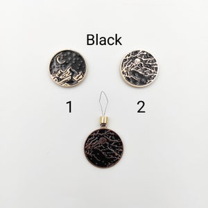 May include: Three circular black and gold metal charms labelled Black. Item 1 features a crescent moon and stars. Item 2 and the bottom charm display a detailed tree branch design. The bottom charm includes a small gold loop with a thin wire threader.