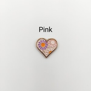 May include: A pink heart-shaped enamel pin with a purple and orange flower design.