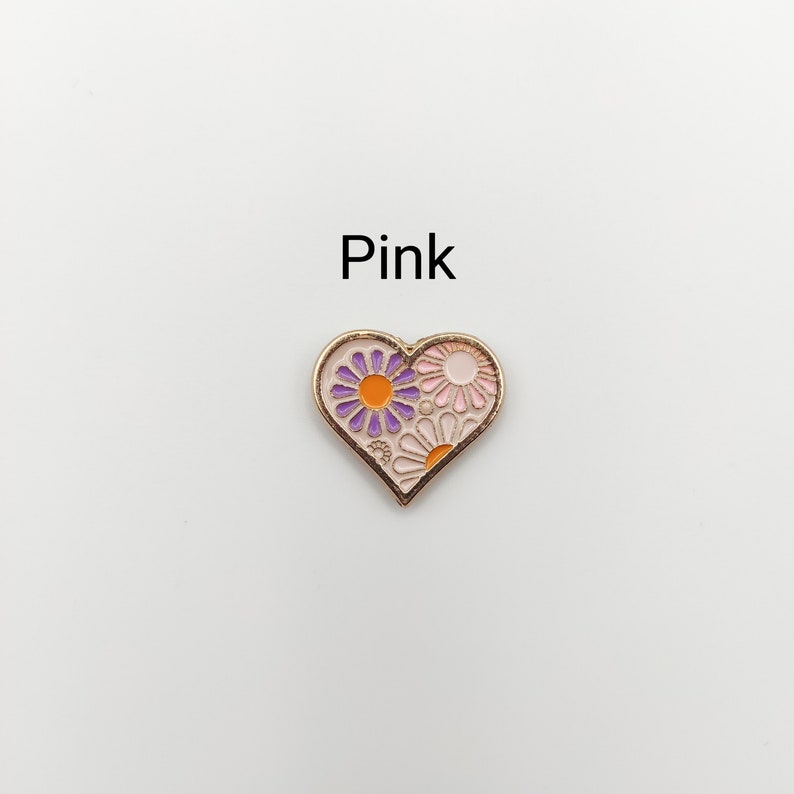 May include: A pink heart-shaped enamel pin with a purple and orange flower design.