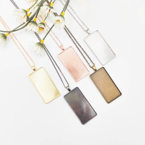 May include: Five different colored rectangular pendant trays with chains. The trays are silver, gold, rose gold, bronze, and black.