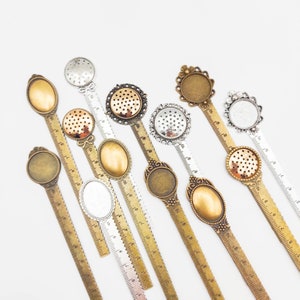 Könnte beinhalten: Sortiment von 12 Metalllinealen mit dekorativen, verzierten, ovalen, leeren, Metallrahmen. Die Lineale sind etwa 15 cm lang und haben eine Skala in Zoll.