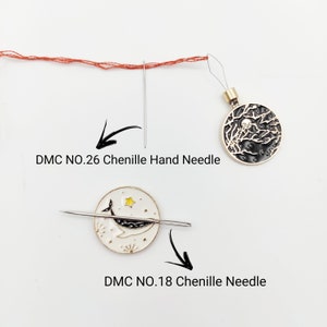 May include: Two round metal needle minders with enamel designs. One features a black night sky with trees and a moon, the other a white background with a whale and star. Includes a DMC NO.26 Chenille Hand Needle and a DMC NO.18 Chenille Needle.