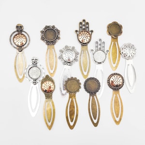 Puede incluir: Surtido de 12 colgantes de marcapáginas de metal en tono plateado y dorado con varios diseños, incluyendo una calavera, una mano y un patrón floral. Cada colgante tiene un inserto de vidrio o plástico transparente para agregar un toque personal.