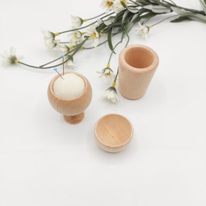 May include: Three wooden containers for sewing supplies. A pincushion with a white fabric top sits on a small pedestal. A small bowl and a taller cylindrical container are also included.