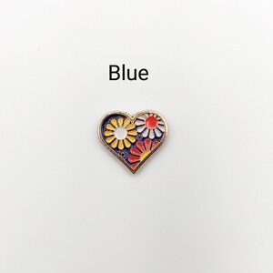 May include: Blue enamel heart-shaped pin with a floral design. The flowers are yellow, red, and white.