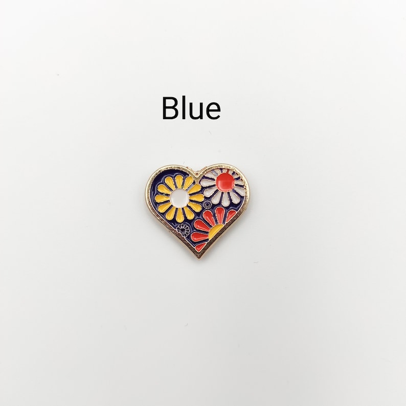 May include: Blue enamel heart-shaped pin with a floral design. The flowers are yellow, red, and white.