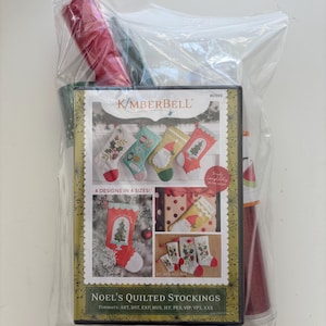 May include: A Christmas-themed craft kit featuring a boxed set of Noel's Quilted Stockings. The box displays four stocking designs with festive patterns. The kit includes red and green fabric rolls, all packaged in a clear plastic bag.