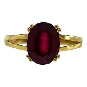 Op de afbeelding: Een gouden ring met een grote, ovaal geslepen, dieprode edelsteen in een zetting met vier pootjes. De ringband is glad en gepolijst, met een gespleten ontwerp dat aansluit op de centrale zetting, wat een levendige, verzadigde karmozijnrode kleur toont.