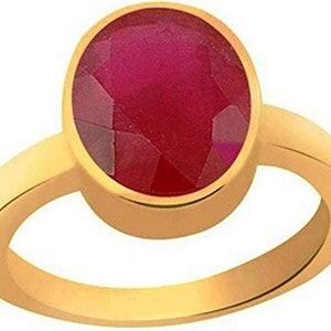 Op de afbeelding: Een gouden ring met een grote, ovaalvormige, gefacetteerde dieprode edelsteen in een gladde, gepolijste gouden band. De steen heeft een levendige karmozijnrode kleur met zichtbare geometrische facetten over het gehele oppervlak van de steen.