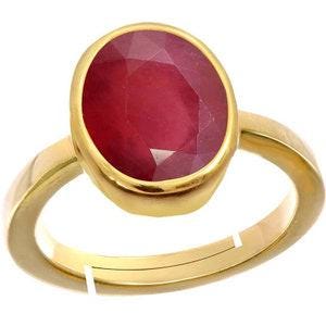 Op de afbeelding: Een gouden ring met een grote, ovaalvormige, gefacetteerde dieprode edelsteen in een gladde zetting. De ringband is van gepolijst goud met een zichtbare opening aan de onderkant, wat duidt op een verstelbaar ontwerp voor een comfortabele pasvorm.