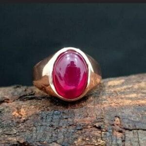 Op de afbeelding: Een gouden ring met een grote, gladde, ovaalvormige cabochon robijn in het midden. De edelsteen heeft een diepe, levendige rode kleur met een gepolijst, reflecterend oppervlak en de ringband is van massief, gepolijst goudkleurig metaal.