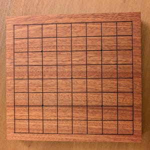 Puede incluir: Un tablero de juego de madera rectangular con una cuadr&iacute;cula de l&iacute;neas negras. El tablero tiene un acabado marr&oacute;n rojizo. La cuadr&iacute;cula est&aacute; formada por l&iacute;neas horizontales y verticales, creando un patr&oacute;n de cuadrados. El tablero es probablemente para un juego de estrategia.
