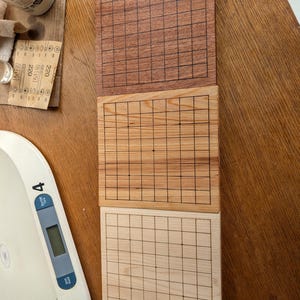 Puede incluir: Tres tableros de juego de Go de madera en diferentes tonos de marr&oacute;n. El tablero superior es de color marr&oacute;n rojizo oscuro, el del medio es de color marr&oacute;n claro y el inferior es de color madera p&aacute;lido. Cada tablero tiene una cuadr&iacute;cula de l&iacute;neas negras.