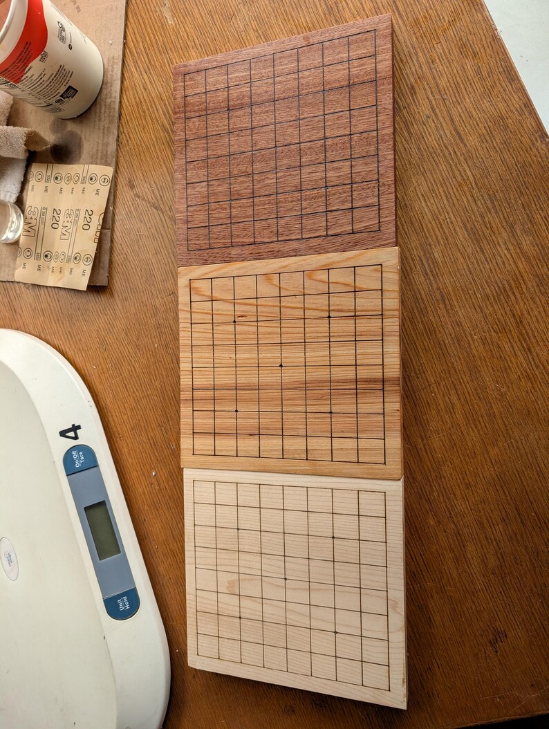 Puede incluir: Tres tableros de juego de Go de madera en diferentes tonos de marr&oacute;n. El tablero superior es de color marr&oacute;n rojizo oscuro, el del medio es de color marr&oacute;n claro y el inferior es de color madera p&aacute;lido. Cada tablero tiene una cuadr&iacute;cula de l&iacute;neas negras.