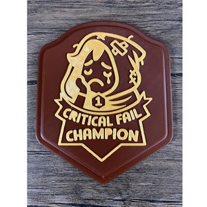 May include: A brown, shield-shaped badge with a gold border and text. The badge features a cartoon illustration of a person with a sad expression and the text "Critical Fail Champion".