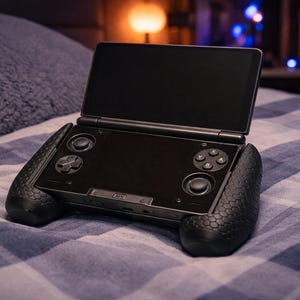 May include: A black handheld gaming console with a dual-screen clamshell design. The device features a top display screen, a bottom screen with integrated directional pads, action buttons labeled A, B, X, and Y, and two analog joysticks.
