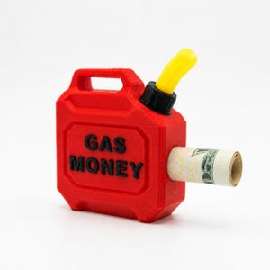 Könnte beinhalten: Ein leuchtend roter Kunststoffbehälter in Form eines Benzinkanisters mit gelbem Ausguss und schwarzem Verschluss. Die Worte GAS MONEY sind in Schwarz auf der Vorderseite eingeprägt. Ein zusammengerollter Dollarschein steckt in der Seitenöffnung.