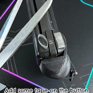 May include: A black gaming controller attachment with an R1 button extension, featuring small pieces of clear adhesive tape applied to the surface. The text Modern problems require modern solutions and Add some tape on the button extensions to prevent slipping are visible.